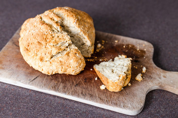 rustic homemade herbs and sesame bread just out of the oven on cutting board with knife and slice cut out