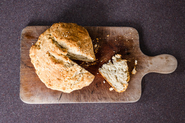 rustic homemade herbs and sesame bread just out of the oven on cutting board with knife and slice cut out