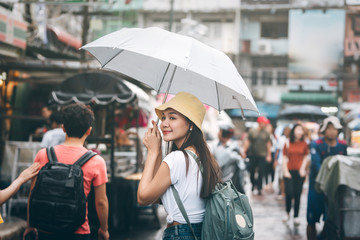 Young adult asian traveller hold umbrella when rainy at walking street.