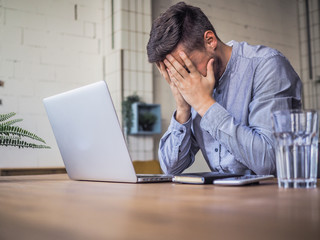 worried and disappointed remote online working man in casual outfit with laptop sitting in an...