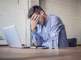 worried and disappointed remote online working man in casual outfit with laptop sitting in an...
