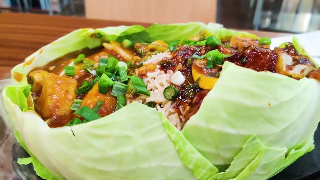 Panning in shot of indian sizzler dish kept on a hot metal plate with stema coming out and filled with vegetabes like rice, tofu, paneer, beans, manchurian and much more.