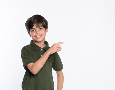 Young boy in green polo shirt standing isolated on white background looking at camera gesturing pointing to side