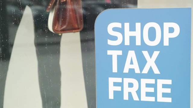 Shop tax free sticker sign in front of store, window reflects people passing nearby. Tourist shopping store without tax.