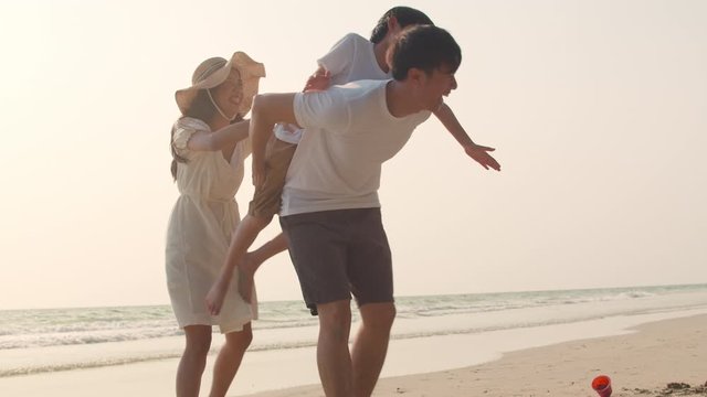 Asian young happy family enjoy vacation on beach in the evening. Dad, mom and kid relax playing together near sea when sunset. Lifestyle travel holiday vacation summer trip concept. 4k slow motion.