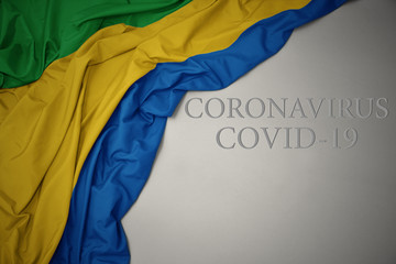 waving national flag of gabon on a gray background with text coronavirus covid-19 . concept.