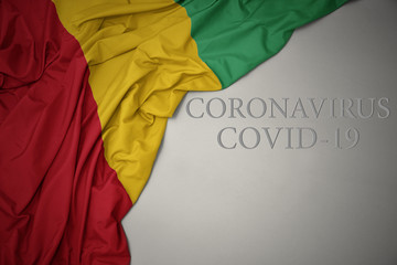 waving national flag of guinea on a gray background with text coronavirus covid-19 . concept.