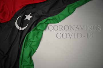 waving national flag of libya on a gray background with text coronavirus covid-19 . concept. - obrazy, fototapety, plakaty