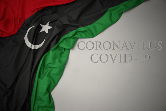 waving national flag of libya on a gray background with text coronavirus covid-19 . concept.