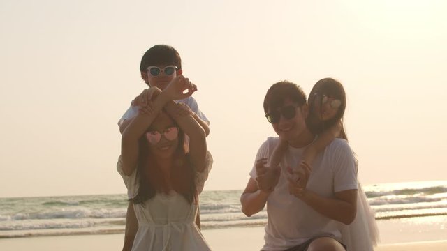 Asian young happy family enjoy vacation on beach in evening. Dad, mom and kid set camera for take photo while relax together near sea when sunset. Lifestyle travel holiday vacation summer. Slow motion