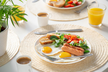 healthy breakfast served on white table (fried eggs, sausages, fresh vegetables and greens, coffee and orange juice)