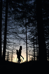Fototapeta na wymiar Silhouettes of loving couple posing in evening forest. Wild nature with amazing views, summer sunset, guy holding girl. Nature, love, happyness concept.
