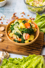 Cooked, steamed or boiled seasonal vegetables in clay ceramic brown bowl pot. Carrot, potato, spinach, cabbage. Vegan, vegetarian low fat diet
