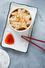 Bowl with korean tteok-bokki or topokki, flatlay on a light-blue stone background, vertical shot