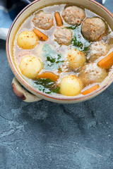 Beige bowl with meatball and potato soup, elevated view on a blue stone surface with space, vertical shot