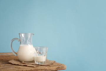 Glassware with fresh milk on table against color background