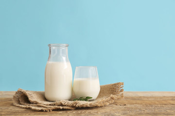 Glassware with fresh milk on table against color background