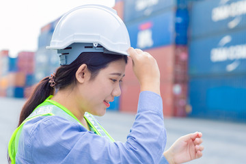 Asian girl teen worker in shipping cargo port work and manage import export goods containers safety with white helmet.