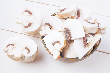 Sliced raw chapminons in and around a wooden bowl on a white wooden background. The concept of healthy food, vegetarianism, mushrooms.
