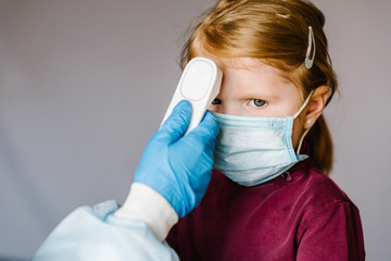 Coronavirus. Nurse or doctor checks girl's body temperature using infrared forehead thermometer...