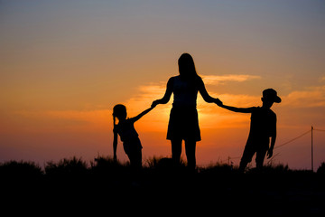 Naklejka na ściany i meble Mother and children hold hands in the background of the sunset.
