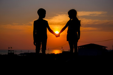 Fototapeta na wymiar Children hold hands in the background of the sunset. Silhouettes of a young boy and girl.