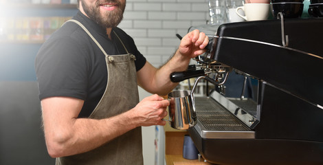 Bearded man barista making coffee on a coffee machine and whips milk with steam. Small business concept