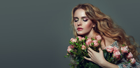 Beautiful tender romantic girl with magnificent wavy blond hair holds a bouquet of pink roses in her hands.