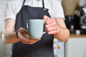 A young barista guy holding a large mug of coffee in his hands. Hands close up