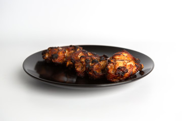 barbecue chicken wings close up on wooden tray shot with selective focus In the black plate, white background