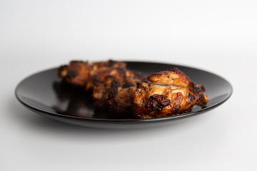 barbecue chicken wings close up on wooden tray shot with selective focus In the black plate, white background