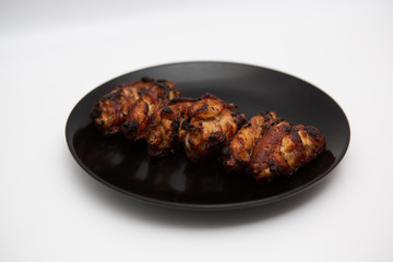 barbecue chicken wings close up on wooden tray shot with selective focus In the black plate, white background