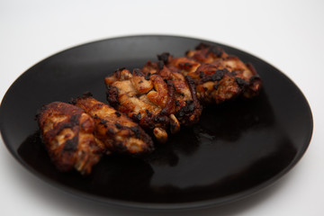 barbecue chicken wings close up on wooden tray shot with selective focus In the black plate, white background