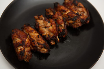 barbecue chicken wings close up on wooden tray shot with selective focus In the black plate, white background