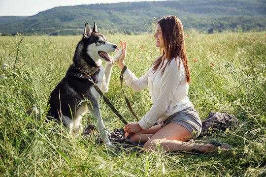 Beautiful woman playing with husky dog outdoors at park.