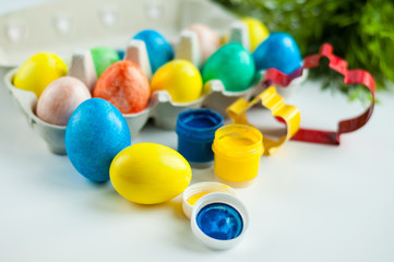 multicolored painted eggs for Easter lie in an egg mold with green twigs in the background and colors