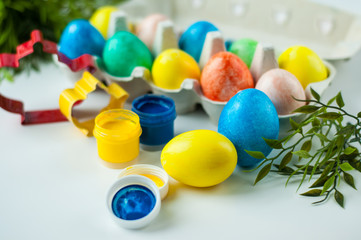 multicolored painted eggs for Easter lie in an egg mold with green twigs in the background and colors