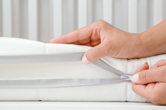 Young woman hand opening cover of new white mattress with zipper. Mother checking hardness and softness of baby bed. Choice of the best type and quality. Closeup.