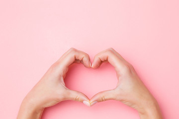 Heart shape created from young woman hands on pastel pink table background. Love and happiness...
