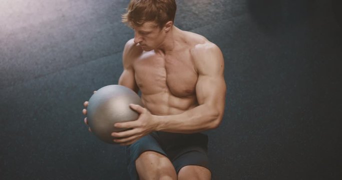 Strong attractive man in the gym doing core ab exercises with a medicine ball, muscular man working out and achieving his goals