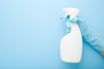 Hand in rubber protective glove holding white spray bottle. Detergent for different surfaces in...