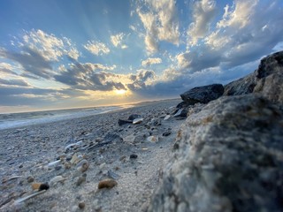 Lido Beach Sunset low to the ground with the shore in focus with the ocean surf, sun, clouds, and sky in the background
