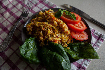 Rise with green spinach and tomatoes on a plate on a white table with a napkin
