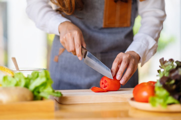 Closeup image of a woman chef cutting and chopping tomato by knife on wooden board