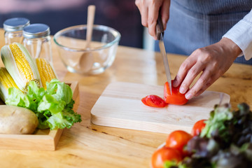 Closeup image of a woman chef cutting and chopping tomato by knife on wooden board