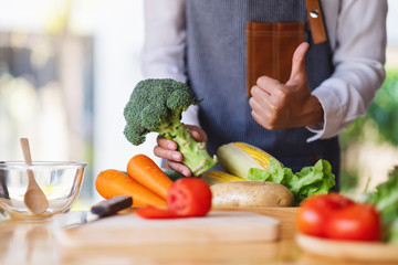 A woman chef holding and making thumb up to show good sign to a green broccoli with vegetables tray on the table