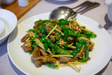 Stir-fried beef with green bell peppers and bamboo shoots on a white plate, with a spoon and fork placed on the side It is a popular Chinese food in Japan.