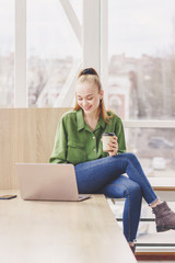 Young beautiful woman sits with a laptop and a cup of coffee