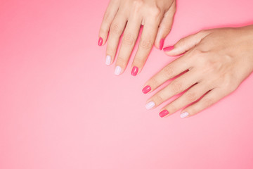 Obraz na płótnie Canvas Closeup top view photography of two beautiful female hands isolated on pastel pink background with empty space for text. Fingernails with modern trendy assymetric two colors design of manicure.