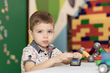 a small boy plays with toys in kindergarten or at home sitting at a table in the children's room
